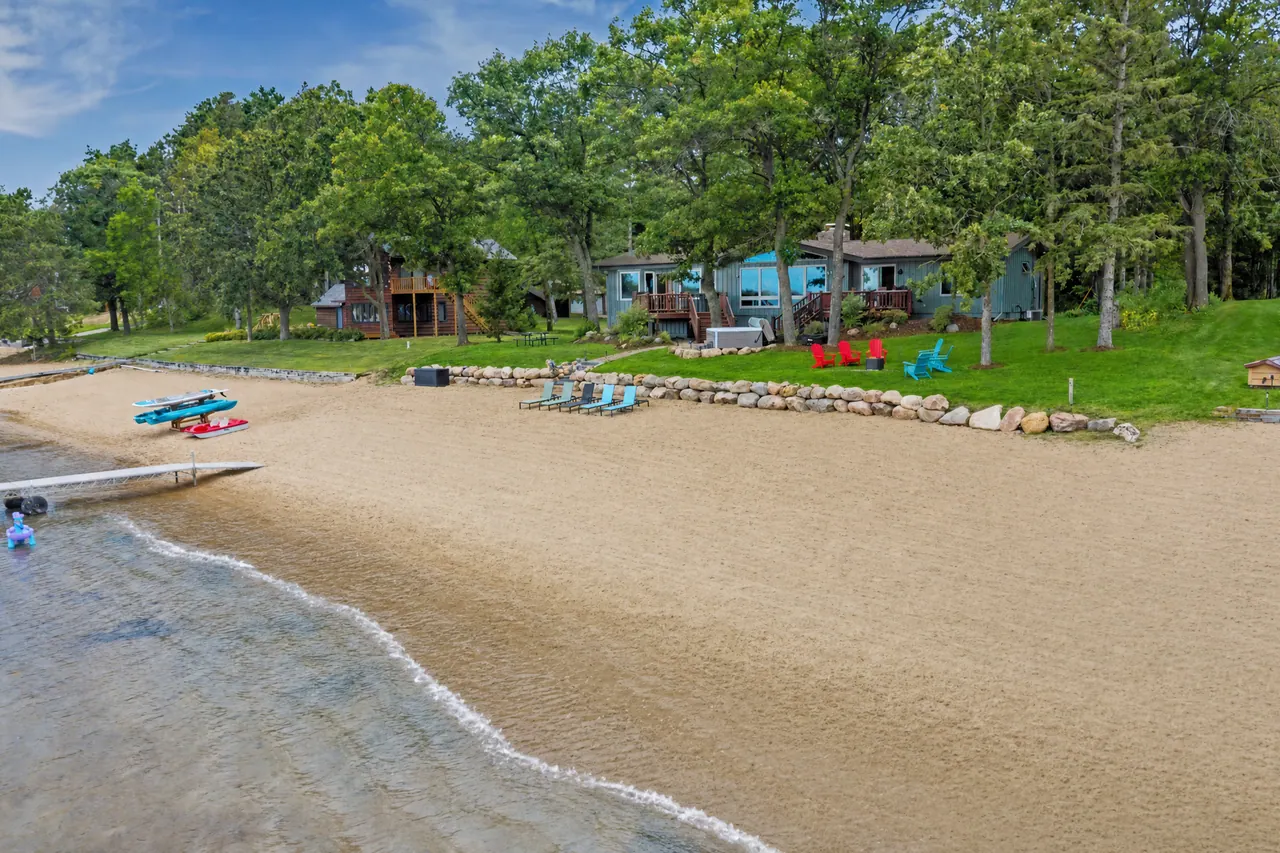 Sandy beach curving along clear, shallow water, with the house in the pines behind it