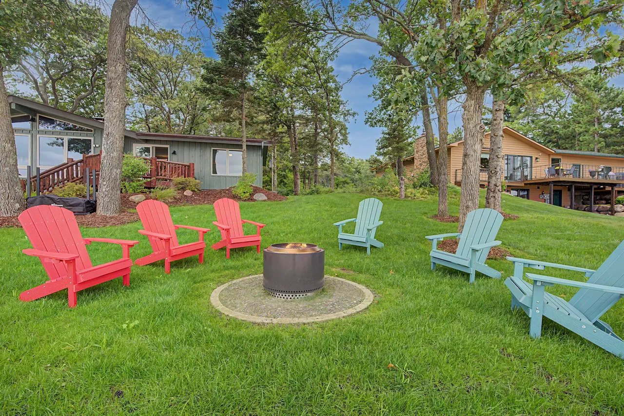 Fire pit circled by red and blue Adirondack chairs