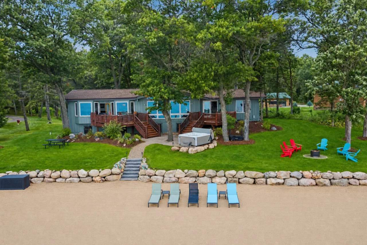 The house from the beach: lounge chairs on the sand, steps up the stone wall, Adirondack chairs on the lawn